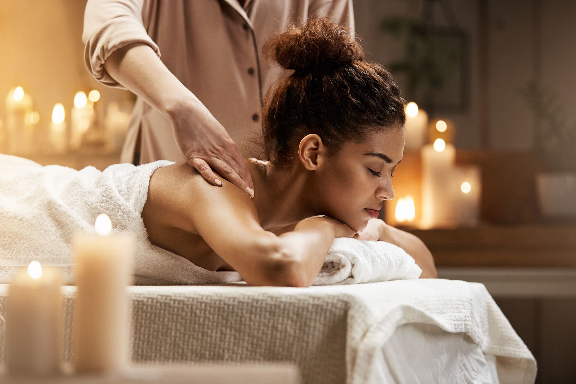 Mulher relaxa durante uma sessão de massagem em ambiente acolhedor e iluminado por velas, ilustrando a proposta de pacotes de hospedagem para a baixa temporada voltados ao bem-estar, que vão além dos descontos e oferecem experiências diferenciadas.