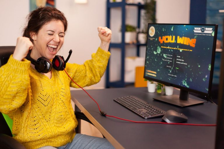 Mulher comemorando vitória em jogo de computador, representando como a gamificação na hotelaria pode engajar e motivar colaboradores, aprimorando sua experiência no ambiente de trabalho.