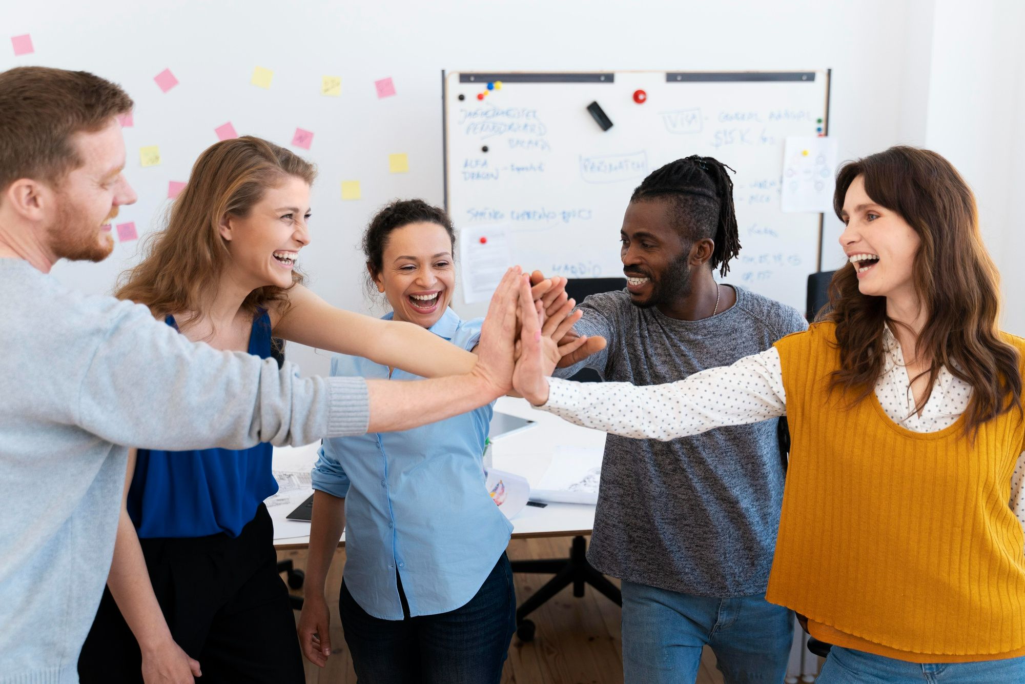 Grupo de colaboradores sorrindo e celebrando com um high five coletivo, ilustrando como a gamificação para treinar equipes pode promover engajamento, colaboração e aprendizado de forma leve e eficaz.