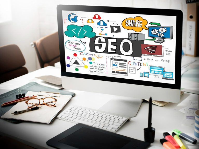 Mesa de trabalho com computador exibindo elementos visuais sobre SEO para sites de hotéis e marketing digital