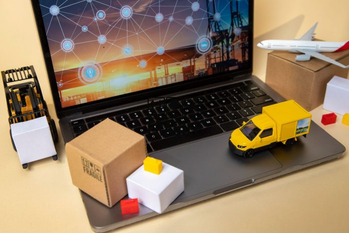 Miniaturas de empilhadeira, caminhão e avião ao redor de um notebook com tela de rede logística, simbolizando a digitalização e integração do controle de estoque em pequenos hotéis.