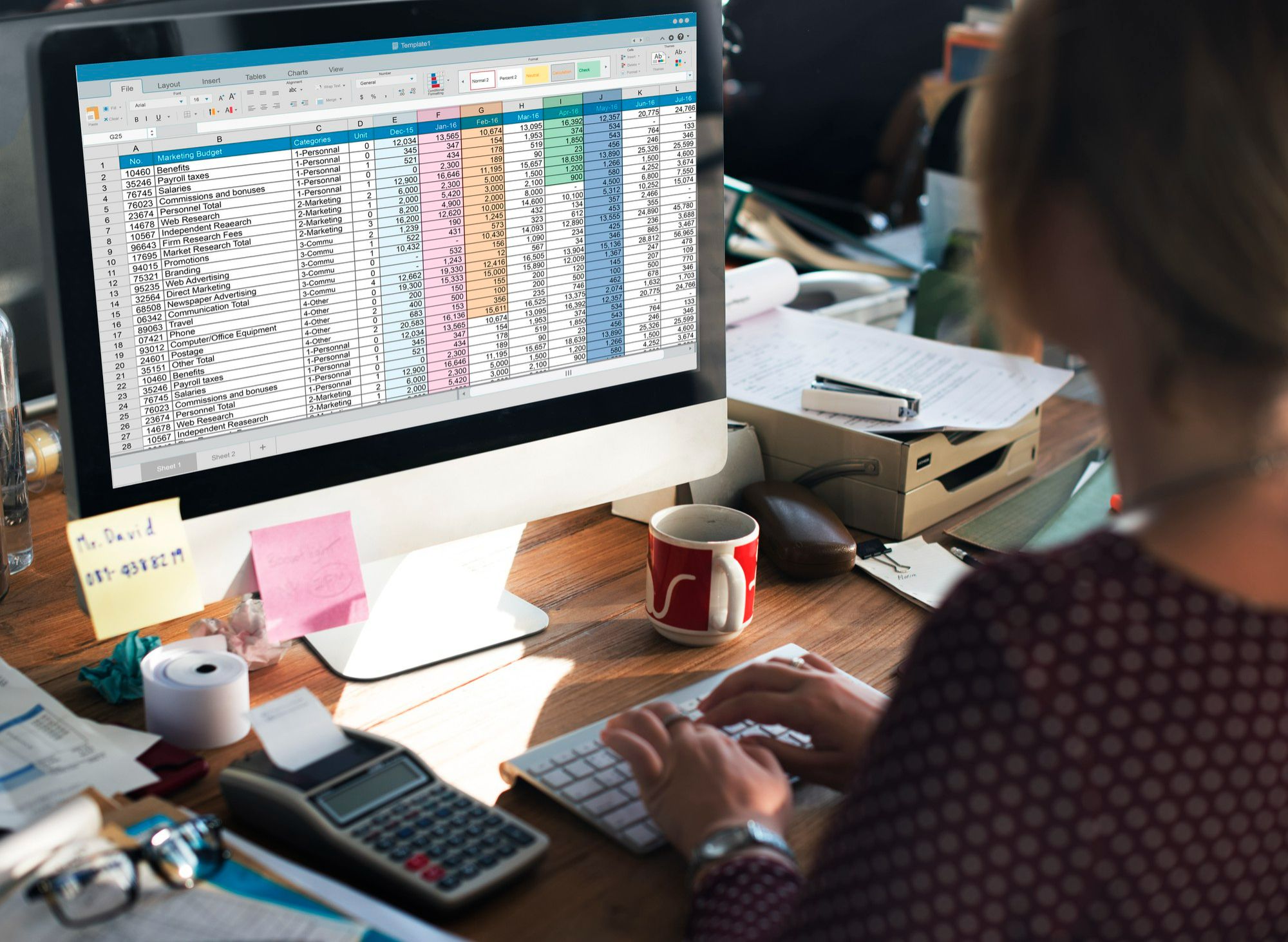 Pessoa trabalhando em planilha de controle de orçamento no computador, em um ambiente de escritório, representando a gestão manual de estoque e finanças em pequenos hotéis.