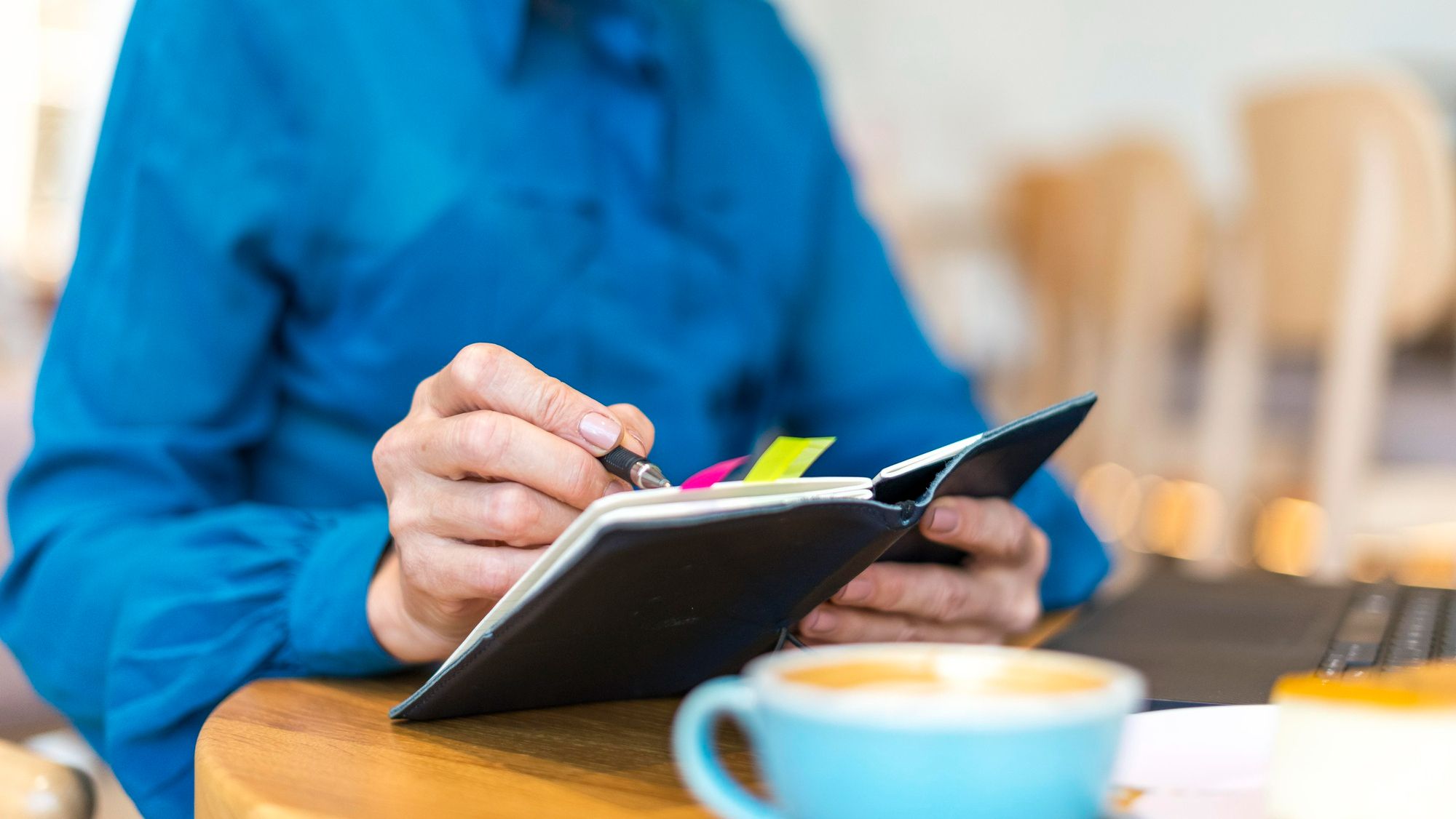 Pessoa fazendo anotações em um caderno com marcadores coloridos, representando o controle manual de estoque ou organização de tarefas em um pequeno hotel.