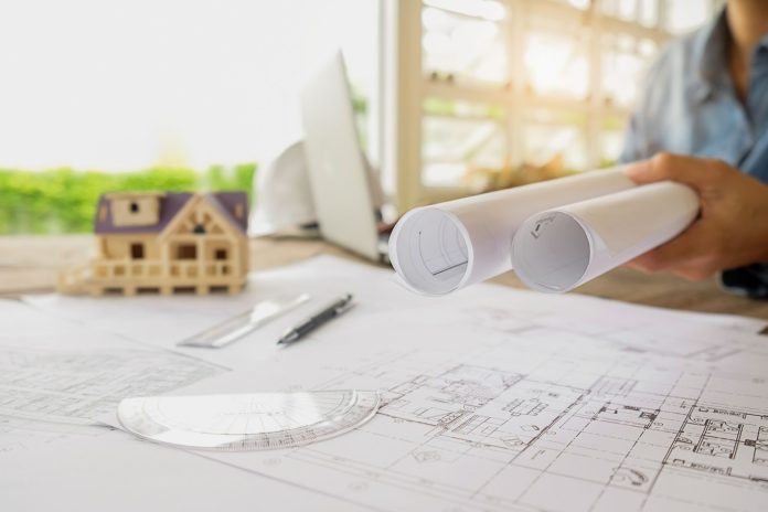 Projeto arquitetônico sobre mesa com planta baixa e maquete de construção ao fundo, representando o planejamento de retrofit com foco em práticas ESG no setor hoteleiro.