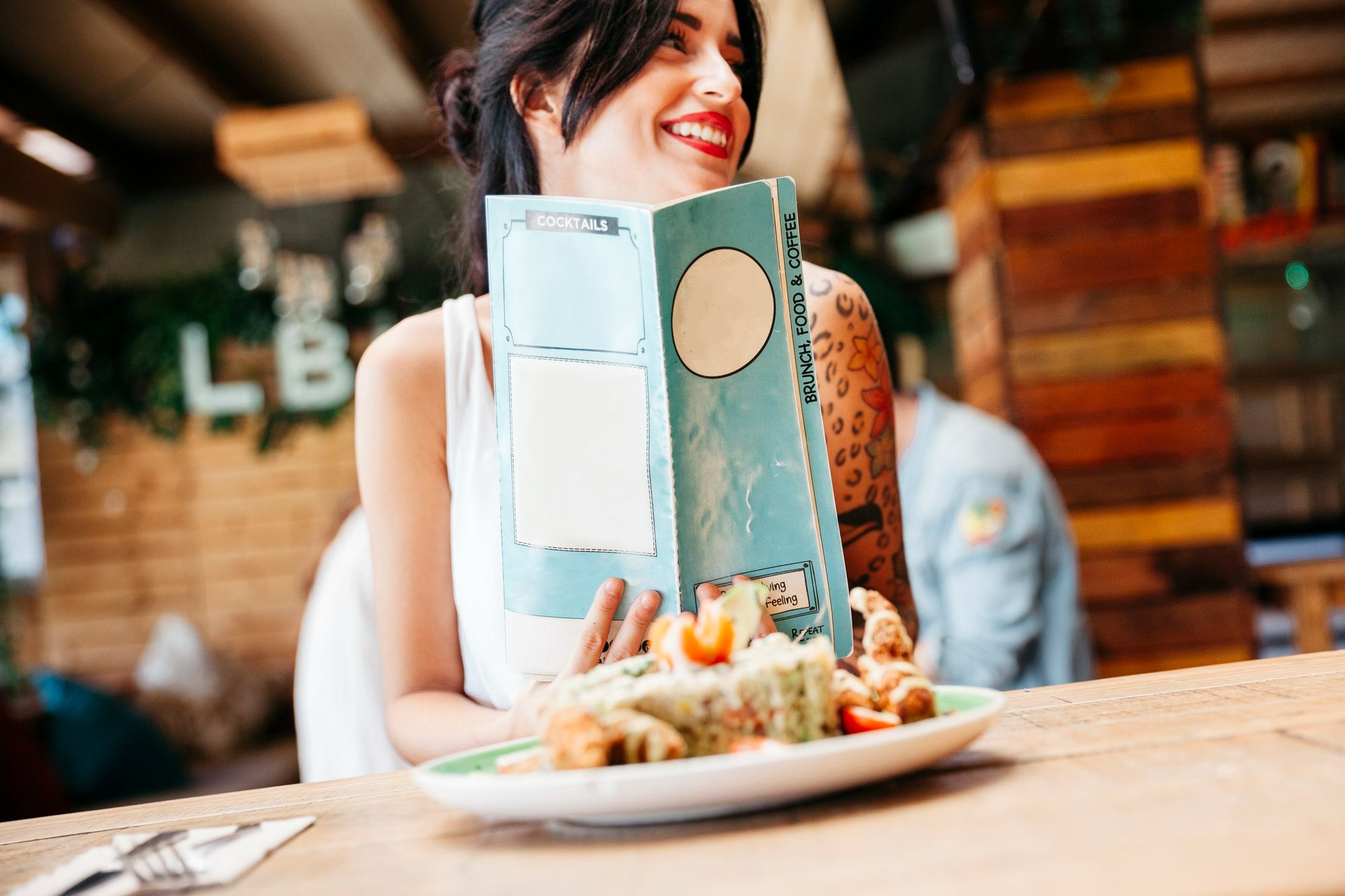 Mulher sorridente com cardápio em mãos e em ambiente de restaurante, simbolizando que é preciso oferecer opções no menu para todos os perfis de clientes. Olhar para a área de Alimentos & Bebidas figura como uma das boas práticas de inclusão em eventos.