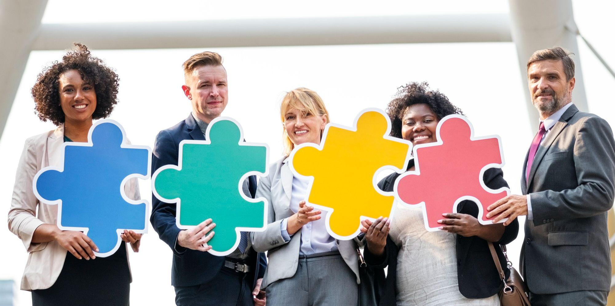 Profissionais diversos segurando peças de quebra-cabeça coloridas, simbolizando como a presença de diferentes perfis de palestrantes e equipes contribui para eventos inclusivos em hotéis.