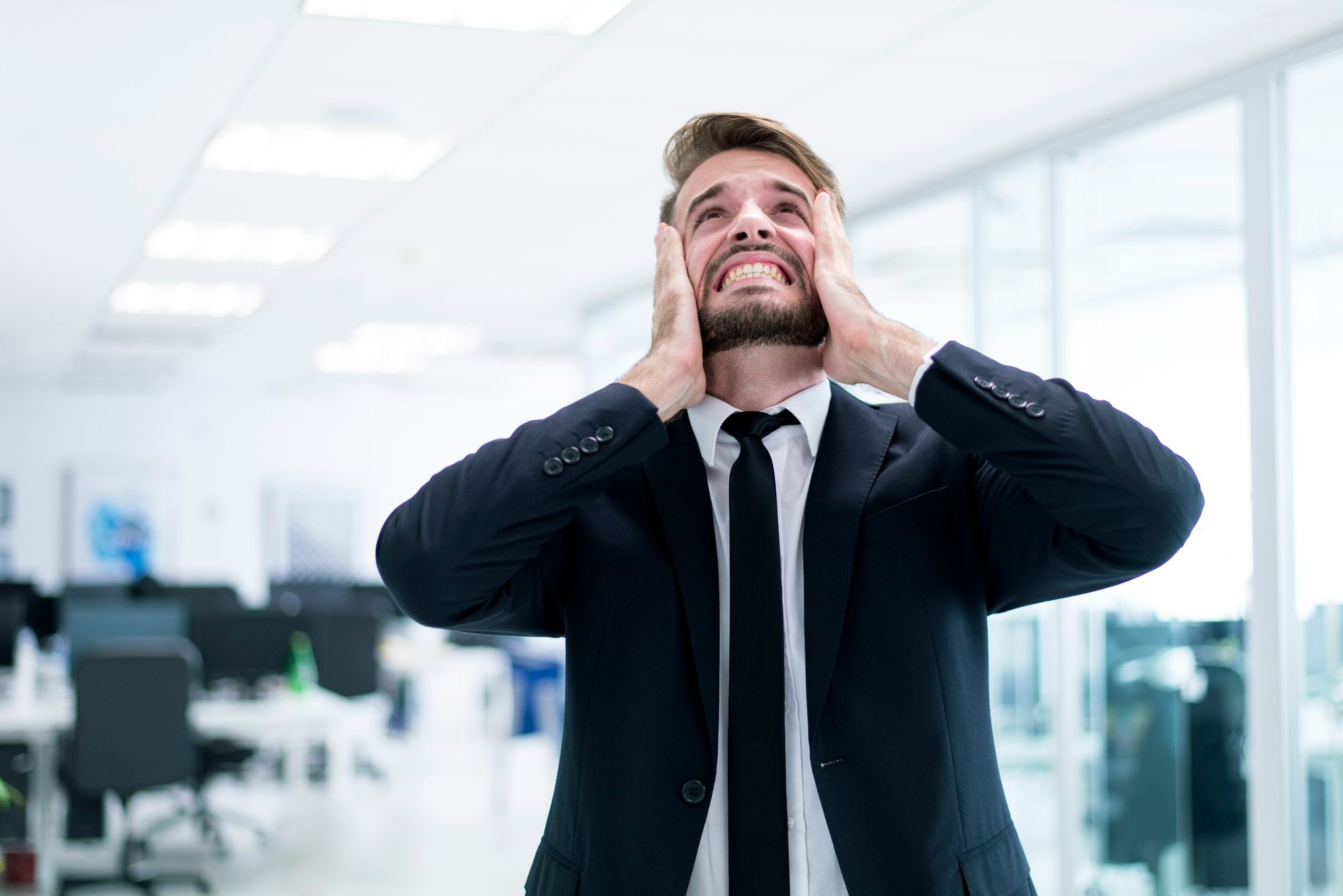 Homem de terno e gravata em um escritório, com expressão de frustração e as mãos no rosto. O objetivo da imagem é representar oportunidades de negócio perdidas devido a erros cometidos em processos de compras para hotéis.