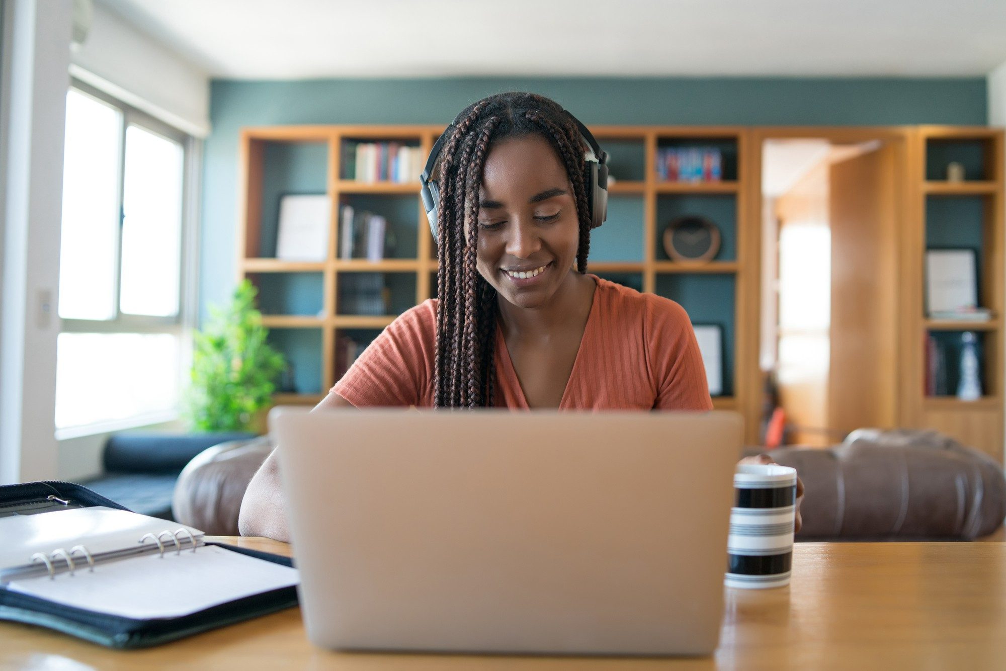 Mulher sentada de frente para o notebook, usando fone de ouvido e sorrindo. O intuito é reforçar que as capacitações, sejam elas online ou presenciais, se enquadram como boas estratégias para restaurantes de hotéis, pois ajudam as equipes a atingirem novos níveis de excelência.
