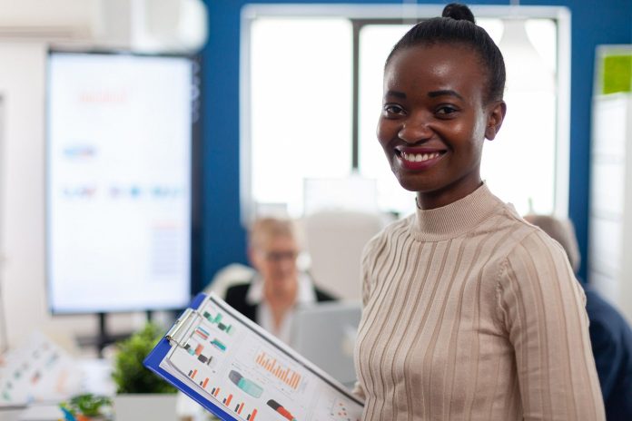 Colaboradora sorridente e em ambiente de escritório, com gráficos em mãos e porte de gestora, simbolizando como os estilos de liderança na hotelaria impactam a motivação e o desempenho das equipes no dia a dia.