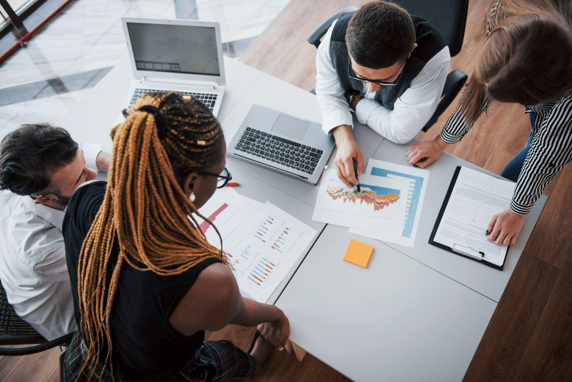 Equipe reunida ao redor de gráficos e relatórios de desempenho, analisando dados para definir estratégias conforme o contexto. A imagem representa a liderança situacional, um dos tipos de liderança em hotéis mais eficazes devido à sua capacidade de adaptação a diferentes cenários para alcançar melhores resultados operacionais.