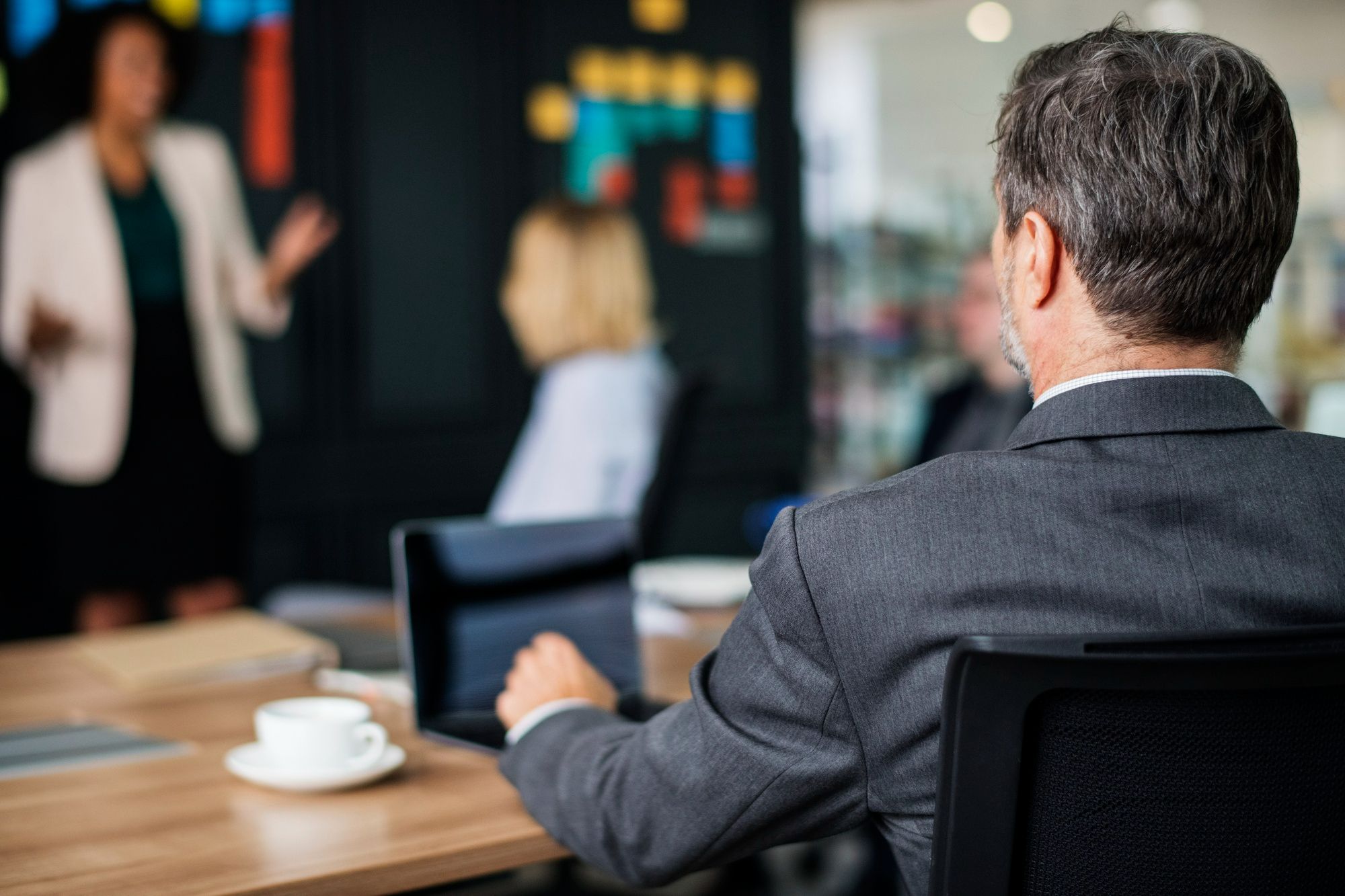 Executivo observa reunião enquanto lidera a equipe com postura decisiva, simbolizando um perfil de liderança em hotéis baseado na centralização e no controle, comum em estruturas mais tradicionais.