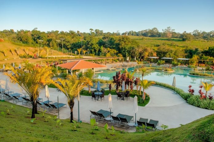 Vista panorâmica da área externa do Cyan Resort by Atlantica, em Itupeva (SP), com extensa área verde, palmeiras, vegetação ornamental e espelho d’água com ilhas ajardinadas. O projeto, assinado pelo Escritório Maria Paula Orlando, é um exemplo de paisagismo na hotelaria que integra natureza, lazer e estética em um ambiente acolhedor.