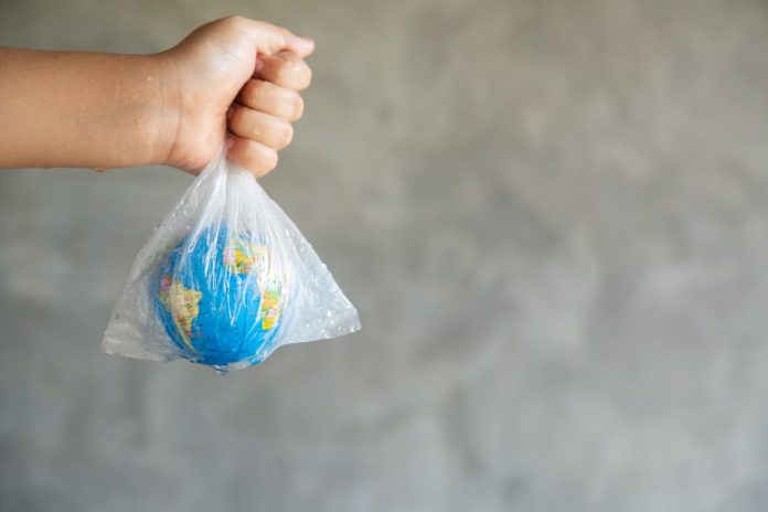 Mão segurando um saco plástico transparente com um globo terrestre dentro, simbolizando o impacto ambiental do uso de plásticos descartáveis. A imagem representa a urgência de medidas sustentáveis, como a redução de plásticos de uso único nos hotéis, um dos objetivos da rede Accor.