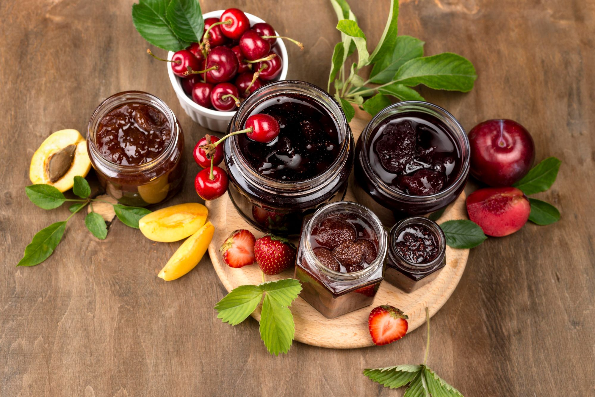 Potes de vidro com geleias artesanais e frutas frescas ao redor, como cerejas, ameixas, morangos e damascos, dispostos sobre uma superfície de madeira. A imagem ilustra uma alternativa sustentável às embalagens plásticas individuais tradicionalmente usadas em hotéis, em linha com o compromisso da Accor de eliminar plásticos de uso único em pontos de contato com o hóspede.