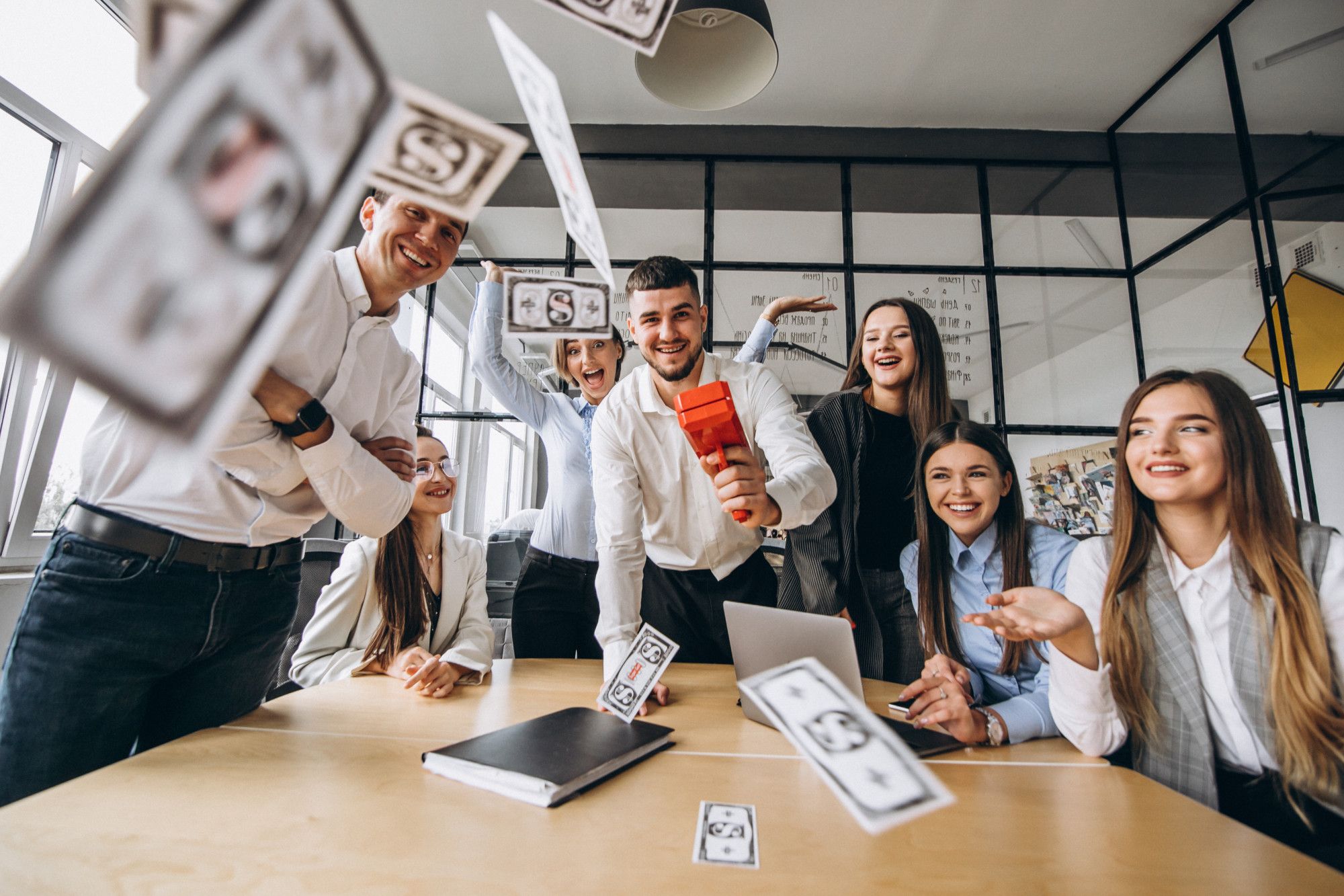 Equipe corporativa animada em escritório, com notas falsas sendo lançadas no ar, simbolizando o sucesso coletivo e a importância de promover treinamentos constantes e soft skills em uma central de atendimento em hotéis.