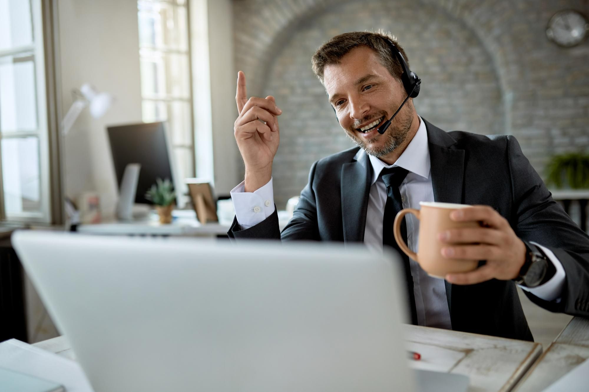Homem de terno usando headset, sorrindo durante uma videoconferência e segurando uma caneca, ilustrando uma abordagem objetiva e focada no contato com leads em inside sales.
