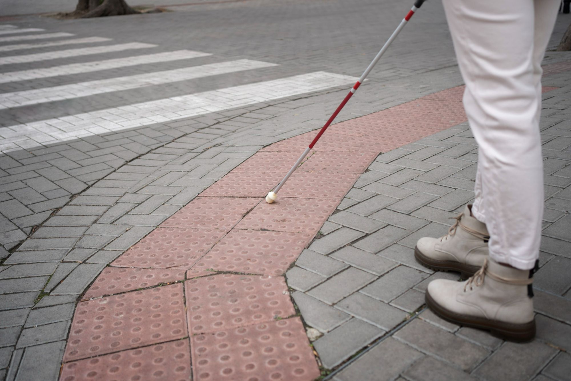 Pessoa caminhando com bengala em calçada adaptada com piso tátil, reforçando que a acessibilidade em hotéis deve contemplar também áreas externas.