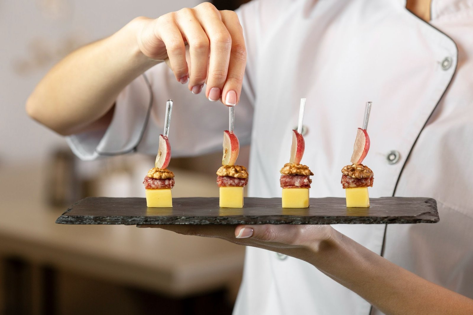 Chef apresenta petiscos elaborados com queijo, nozes, embutidos e fatia de maçã em uma bandeja de degustação, ilustrando a importância de sessões práticas de degustação no treinamento da equipe de restaurante. 