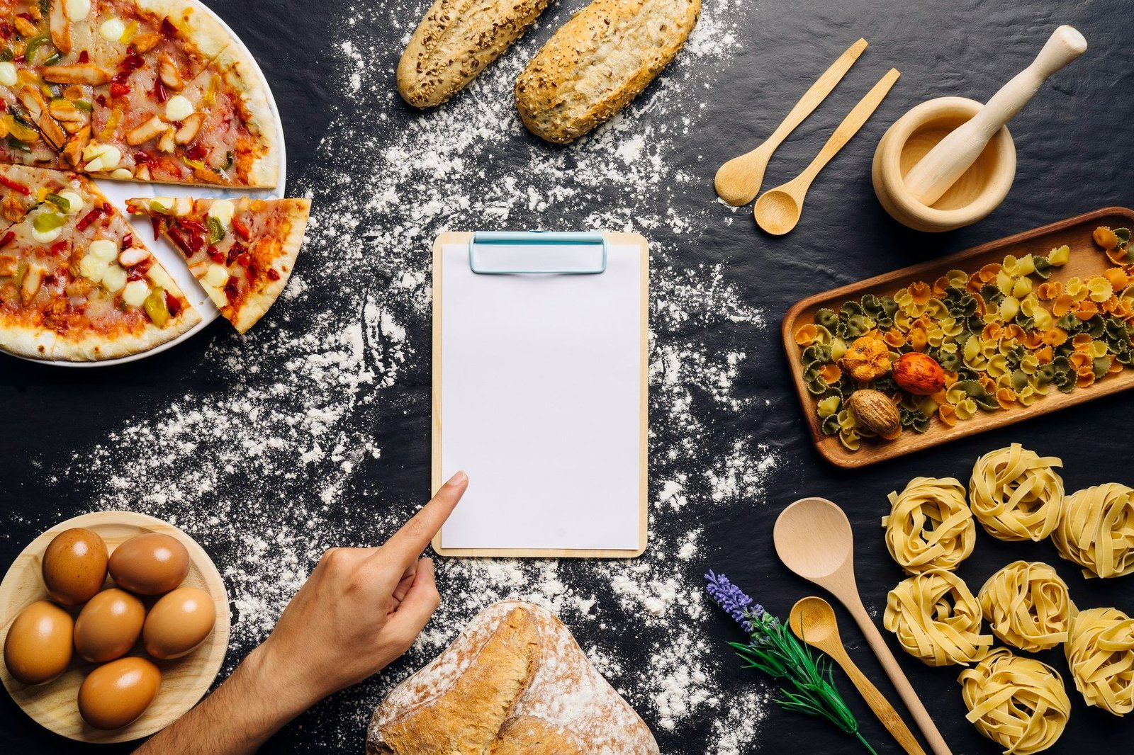 Prancheta em branco cercada por pizza, pães, massas e ovos sobre mesa enfarinhada. Um dedo indicador aponta para a prancheta, simbolizando a atualização periódica do cardápio e a necessidade de manter a equipe informada para garantir excelência no atendimento.