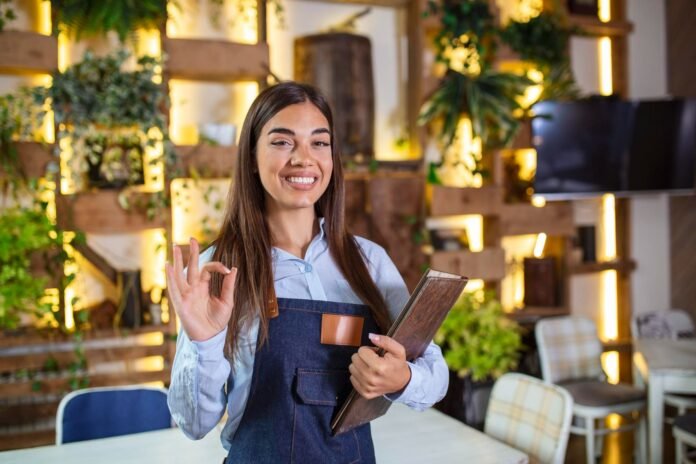 A imagem mostra uma mulher sorrindo, fazendo um sinal de 