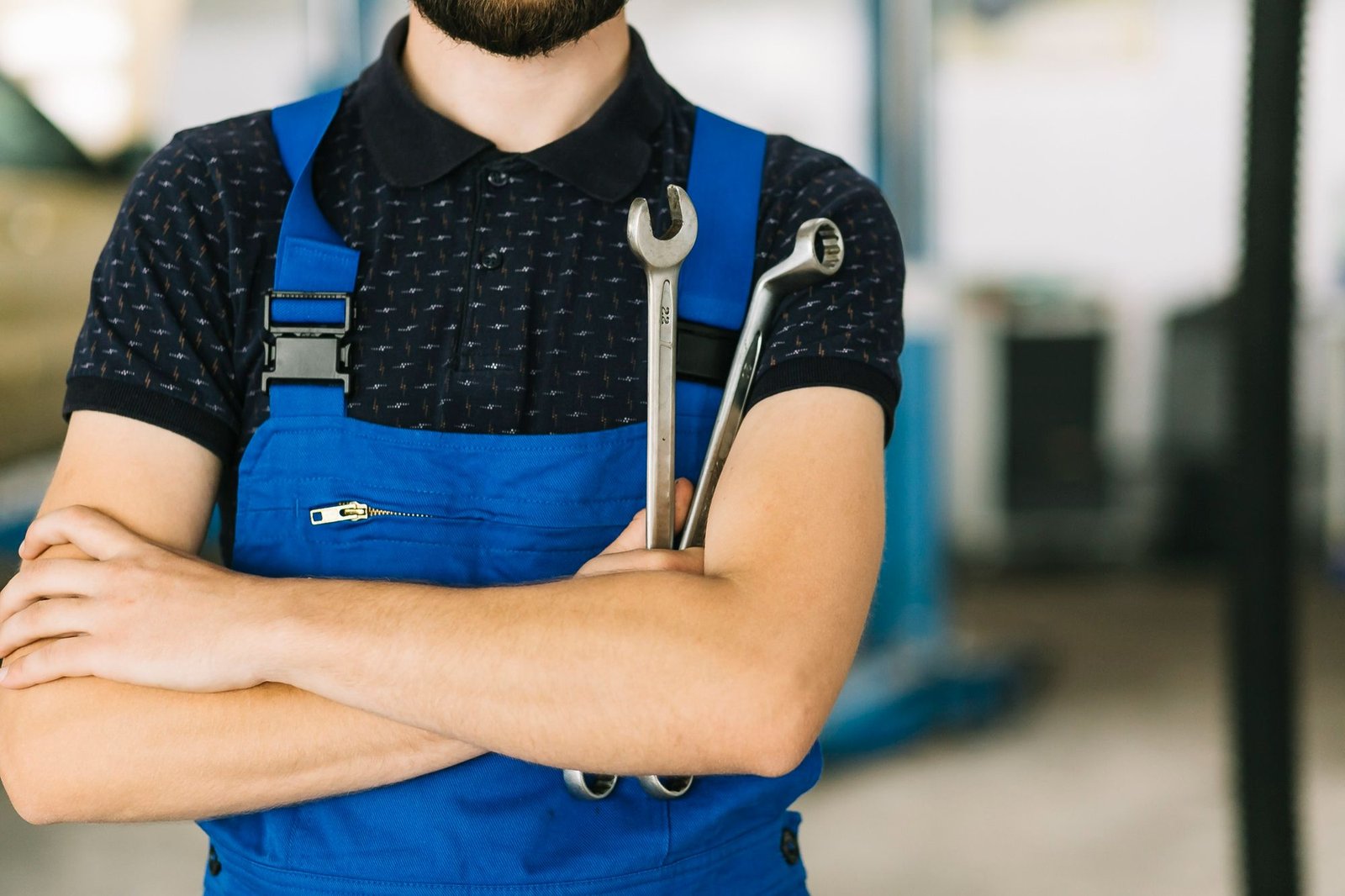 Um profissional de manutenção, vestindo macacão azul e camisa polo escura, de braços cruzados e segurando duas chaves de fenda nas mãos. Ele representa a equipe qualificada e preparada para a execução de um plano de manutenção em hotéis.