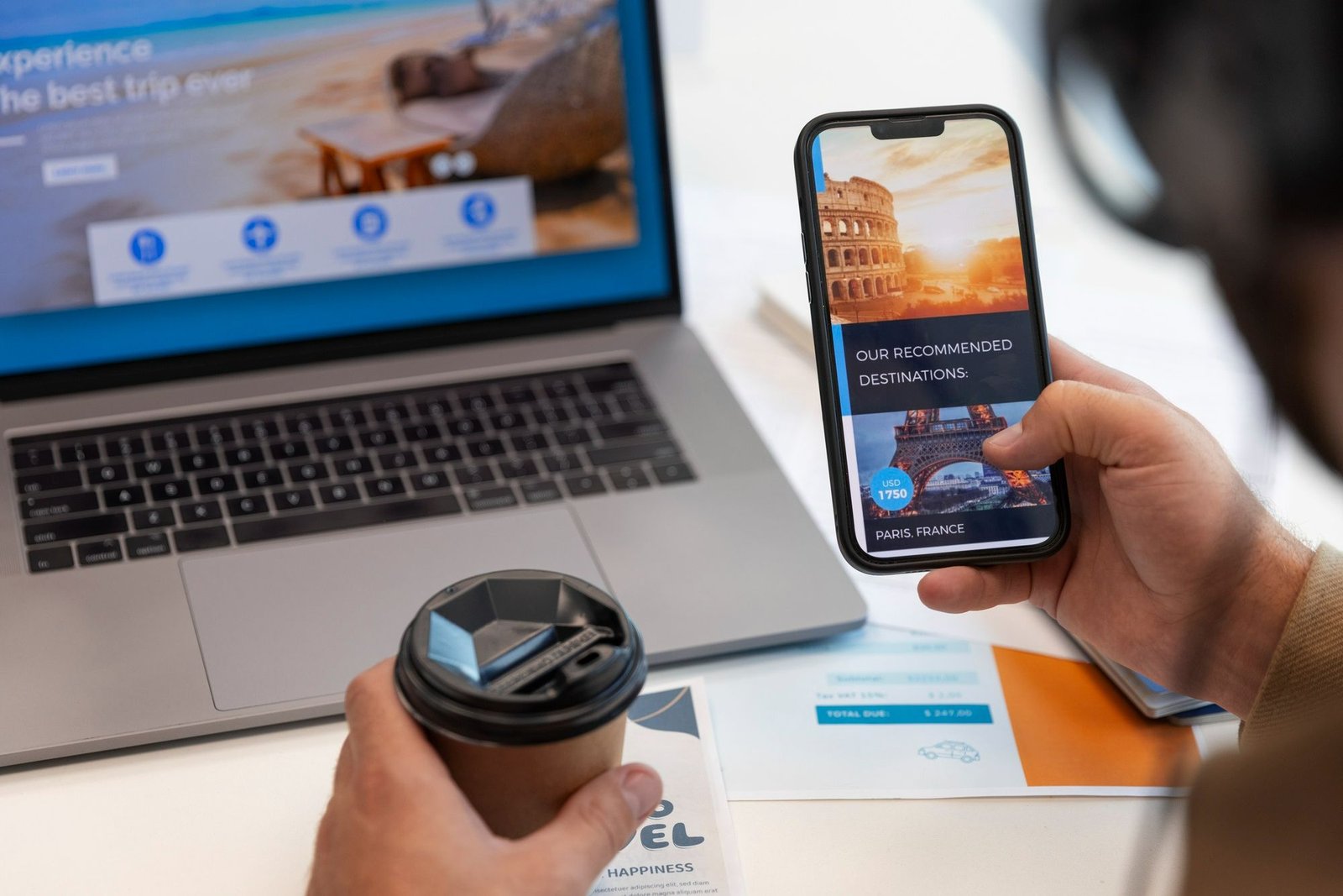 Visão em primeiro plano de um celular exibindo imagens de viagem e a frase "Nossas destinos recomendados". A pessoa segura um copo de café e, ao fundo, há um laptop com um site de viagens aberto. O objetivo é mostrar que parte do trabalho pós-reservas em hotéis é compartilhar dicas de viagem com o visitante, a fim de mantê-lo engajado, já que isso ajuda a evitar no-show em hotel.