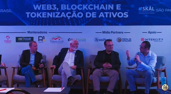 Quatro homens em um painel de discussão sentados em cadeiras de estofado cinza em um palco. O plano de fundo é um banner azul com o título em letras brancas: 