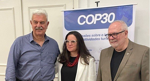 Walter Teixeira, Jaqueline Gil e Aristides Cury posam para foto em frente a um banner do evento sobre a COP30.