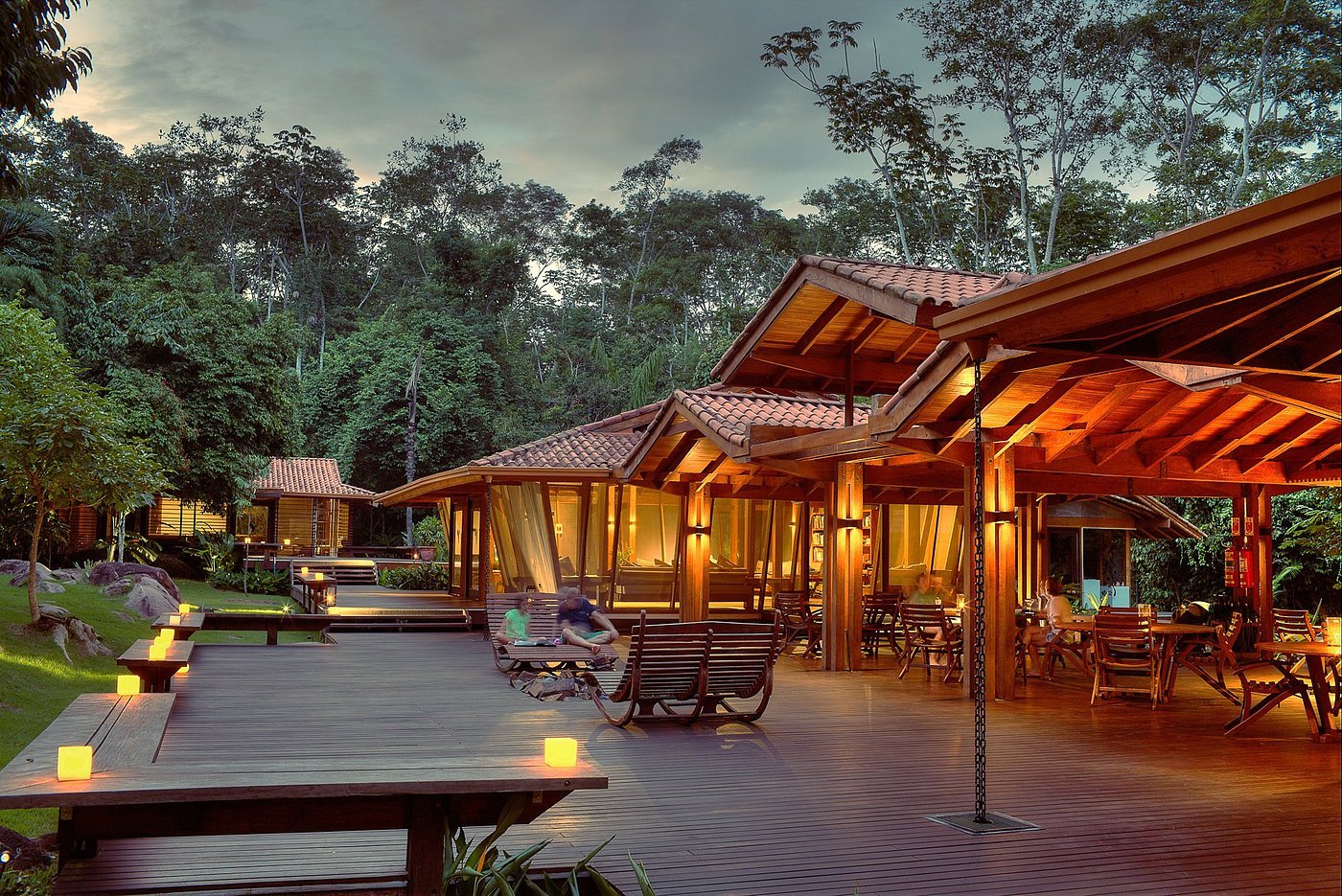 Deck principal do Cristalino Lodge na Amazônia, evidenciando o conceito de luxo sustentável e imersão na selva. A iluminação suave e a arquitetura aberta em madeira convidam ao relaxamento e à observação da natureza. A imagem transmite uma atmosfera de exclusividade e profundo respeito ao meio ambiente.