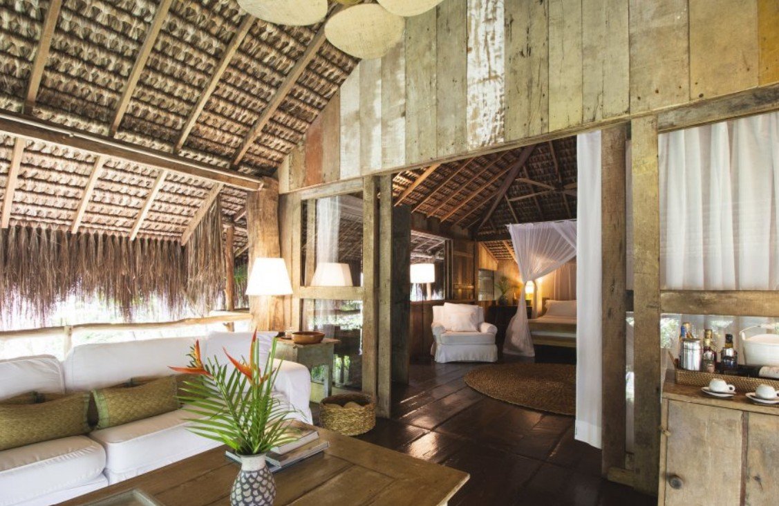 Vista interna da Casa da Árvore do UXUA Casa Hotel & Spa, destacando a arquitetura rústica e sustentável característica de Trancoso. A imagem mostra a integração harmoniosa entre o interior e a natureza externa, utilizando materiais locais como madeira reaproveitada e palha. O ambiente transmite uma sensação de refúgio orgânico, exclusivo e artesanal.