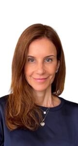 Retrato em primeiro plano de Juliana Carrillo Vieira, autora do texto. Ela tem cabelos castanhos longos e está usando uma blusa escura e colares delicados.