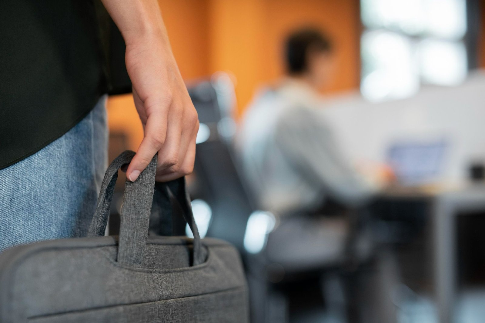 Fotografia em close de um profissional segurando uma pasta de trabalho cinza, simbolizando prontidão e movimento. O cenário de escritório ao fundo reforça o contexto de ambiente corporativo e networking.