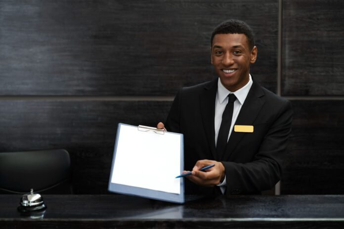 Recepcionista de hotel sorridente oferecendo uma prancheta para check-in. A imagem transmite uma recepção hoteleira acolhedora e profissional, destacando o momento de boas-vindas ao hóspede no balcão de atendimento.