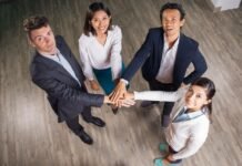 Unir para evoluir: os temas que reforçaram o associativismo em 2025 Vista aérea de quatro profissionais (dois homens e duas mulheres) vestindo roupas sociais e sorrindo para a câmera. Eles estão em círculo e com as mãos sobrepostas no centro, simbolizando o trabalho em equipe e a força do associativismo na hotelaria.