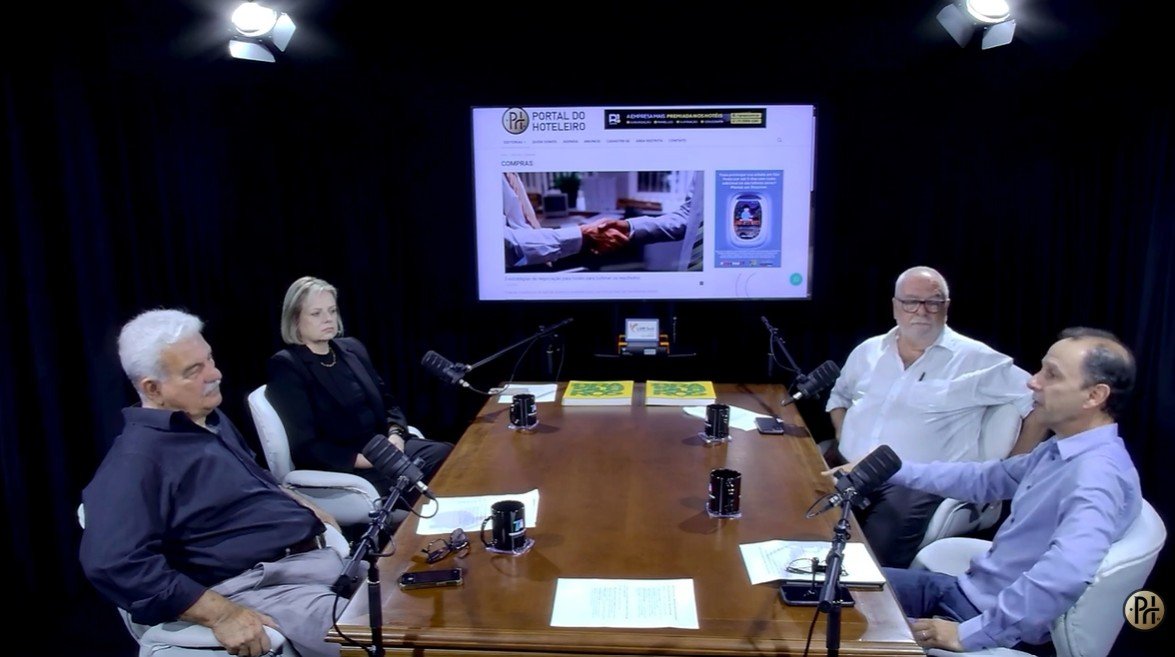 Registro da gravação do videocast do Portal do Hoteleiro sobre compras colaborativas. Quatro especialistas debatem as vantagens da plataforma Solution4Hotel em um estúdio profissional. No centro, uma tela exibe conteúdos sobre estratégias de negociação e compras na hotelaria.