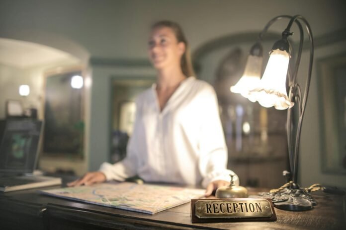 Uma recepcionista de hotel em pé atrás de um balcão de madeira clássico com uma placa de 