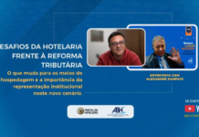 Da escala 6×1 a “Brasil líder de ponta”: entrevista com Alexandre Sampaio mostra valor real do associativismo no turismo Banner digital azul do Portal do Hoteleiro com o título "Os desafios da hotelaria frente à Reforma Tributária". O texto complementar destaca: "O que muda para os meios de hospedagem e a importância da representação institucional neste novo cenário". No centro, duas janelas sobrepostas mostram os participantes de uma videoconferência. À esquerda, Luiz Henrique Miranda, gestor do portal, sorri. Ele usa óculos e blusa vermelha. À direita, Alexandre Sampaio, de terno e gravata, acenando com a mão. Na parte inferior constam os logotipos do Portal do Hoteleiro e da ABIH, além do aviso de que a entrevista está disponível no canal do YouTube.