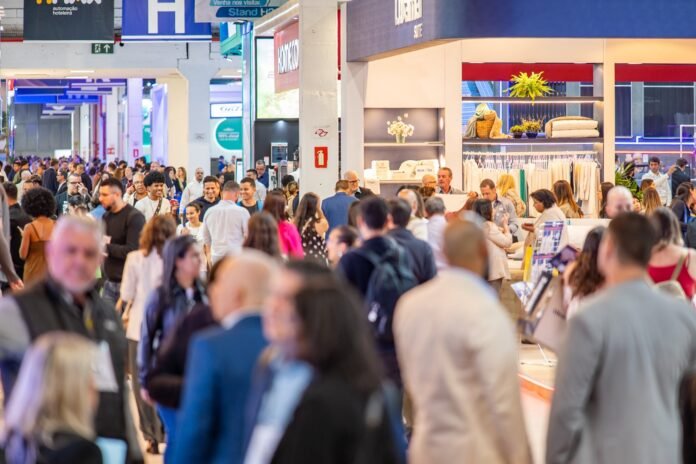 Corredor movimentado durante a edição de 2025 da Equipotel, a principal feira de negócios para hotéis do país. O local está repleto de visitantes e profissionais do setor percorrendo estandes de fornecedores, que expõem desde enxovais a soluções em automação e iluminação.