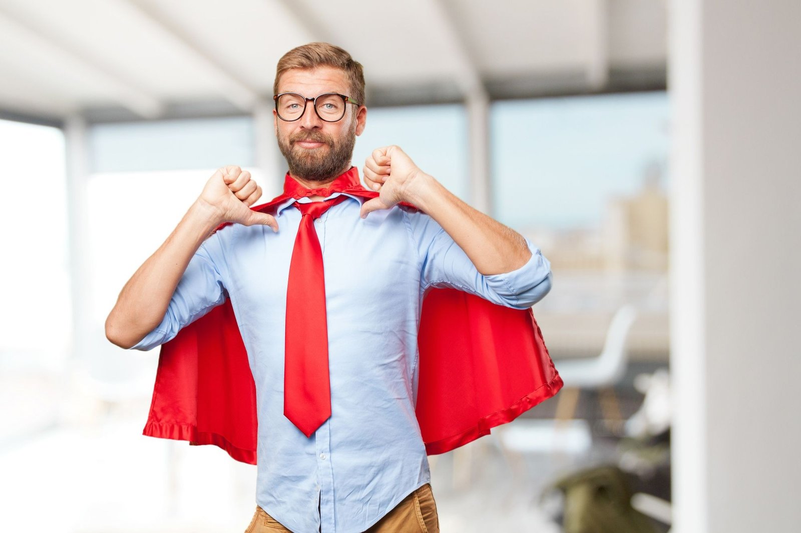Homem vestindo camisa social, gravata e capa vermelha de super-herói aponta os polegares para si mesmo. A imagem ilustra a figura do colaborador que resolve problemas no improviso devido a falhas no controle de estoque.