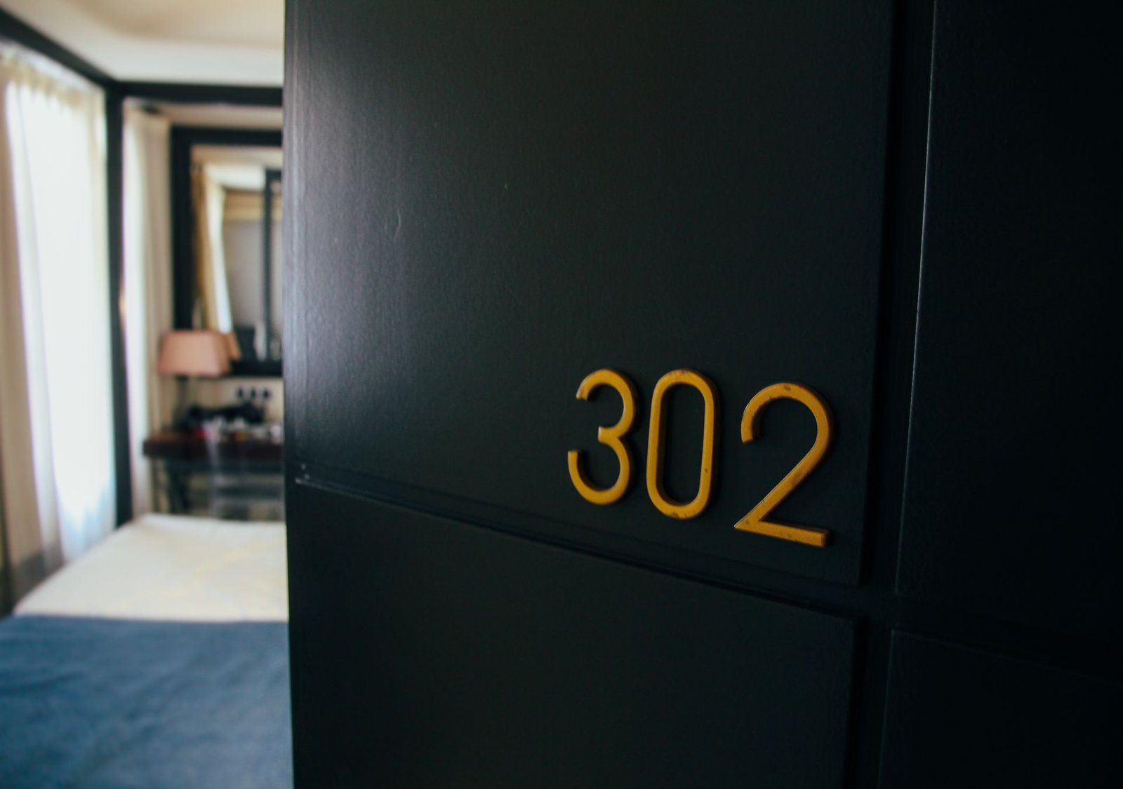 Porta de quarto de hotel azul-escura com o número 302 em amarelo e o interior desfocado, simbolizando uma acomodação interditada para venda devido a problemas com manutenção.