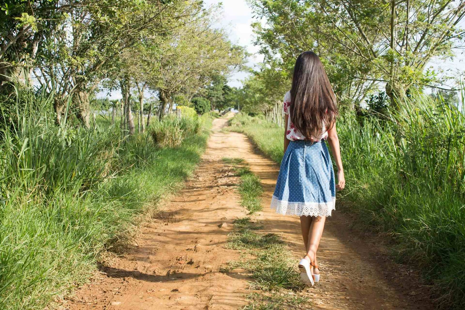 Mulher de costas caminhando por uma estrada de terra cercada por árvores e vegetação, simbolizando a busca por autenticidade e a conexão genuína com o destino no turismo sinestésico.
