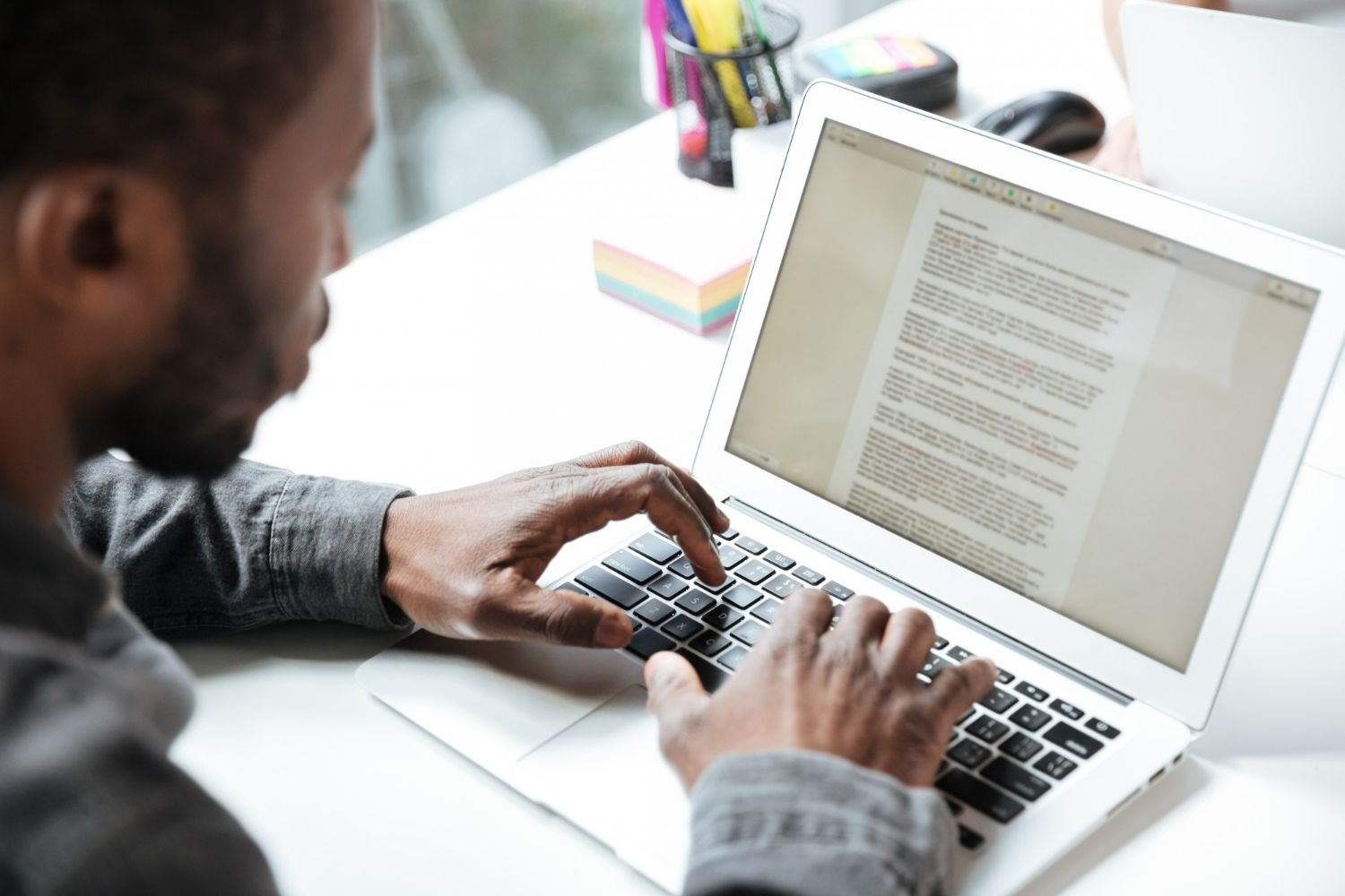Visão parcial de um homem digitando em um notebook em um ambiente que parece ser corporativo. A foto simboliza a aplicação de técnicas de copywriting e o uso de gatilhos mentais para diferenciar o meio de hospedagem da concorrência e aumentar as reservas diretas.