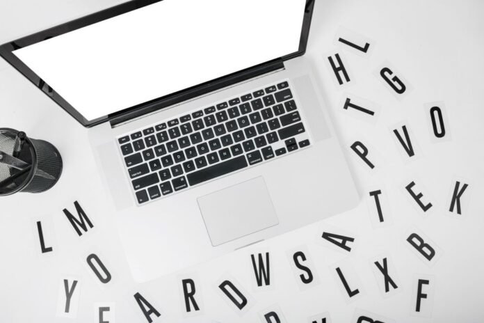 Vista superior de um notebook em uma mesa branca, cercado por letras soltas. A imagem representa a escolha estratégica de palavras na produção de conteúdo, a fim de atrair hóspedes e aumentar as reservas diretas.