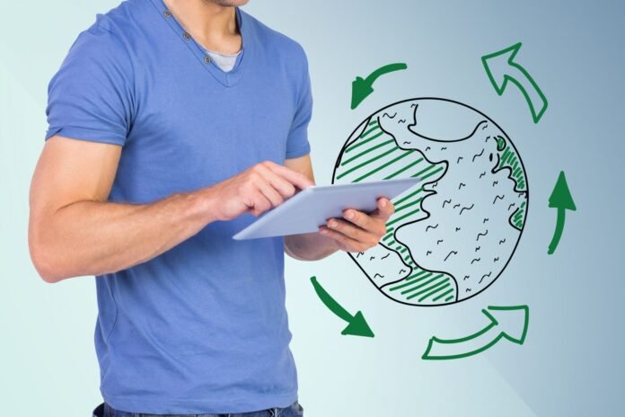 Homem de camiseta azul segura um tablet ao lado de uma ilustração do planeta Terra rodeado por setas verdes de reciclagem, representando o planejamento do setor de Compras e as práticas de sustentabilidade em hotéis.
