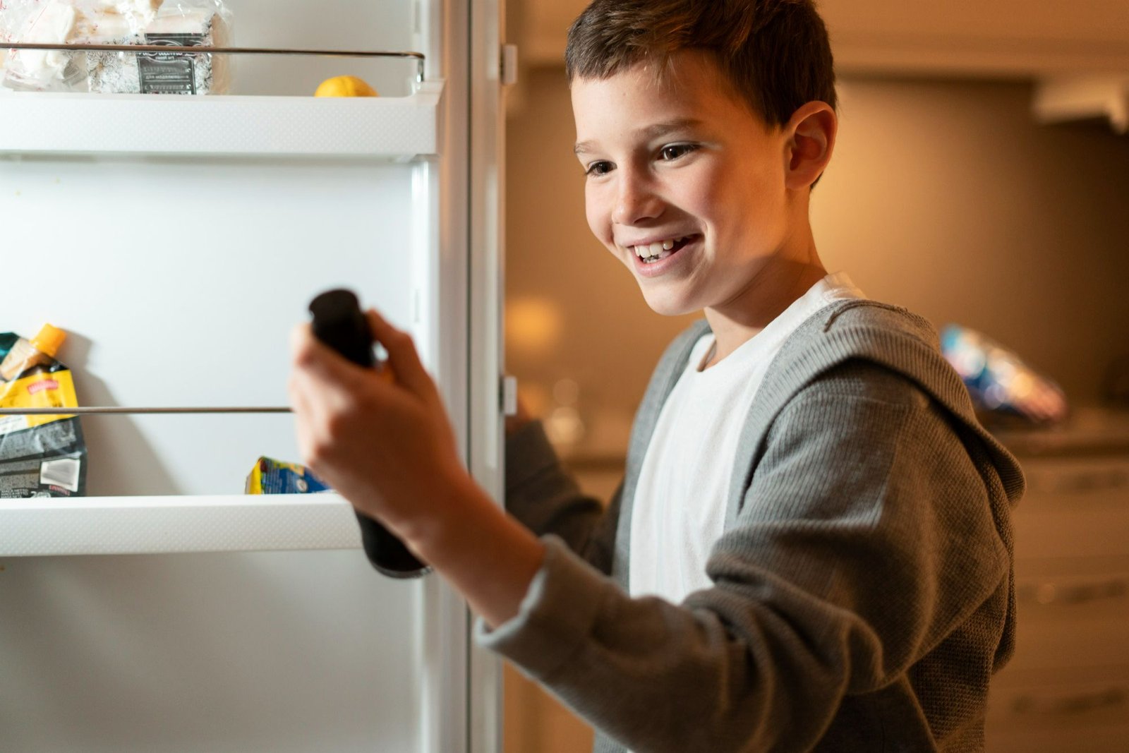 Menino sorrindo ao pegar uma bebida dentro de uma geladeira aberta, a qual representa um frigobar em hotel. 